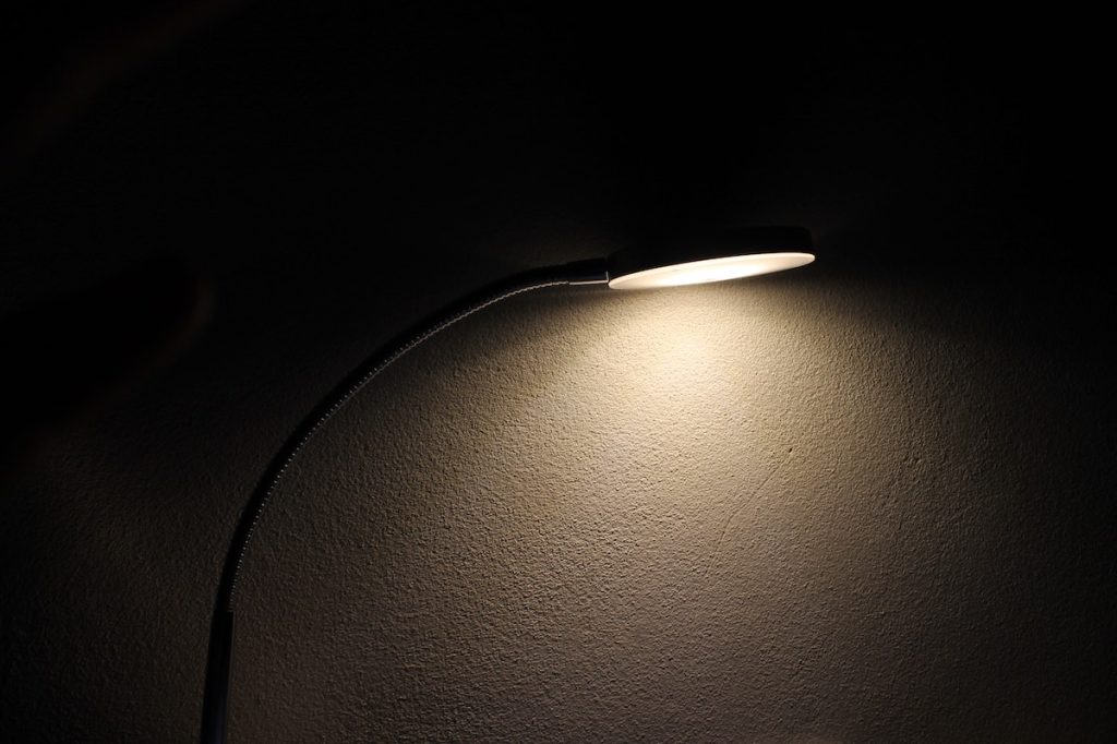 A lamp lit against a blank wall casting shadows