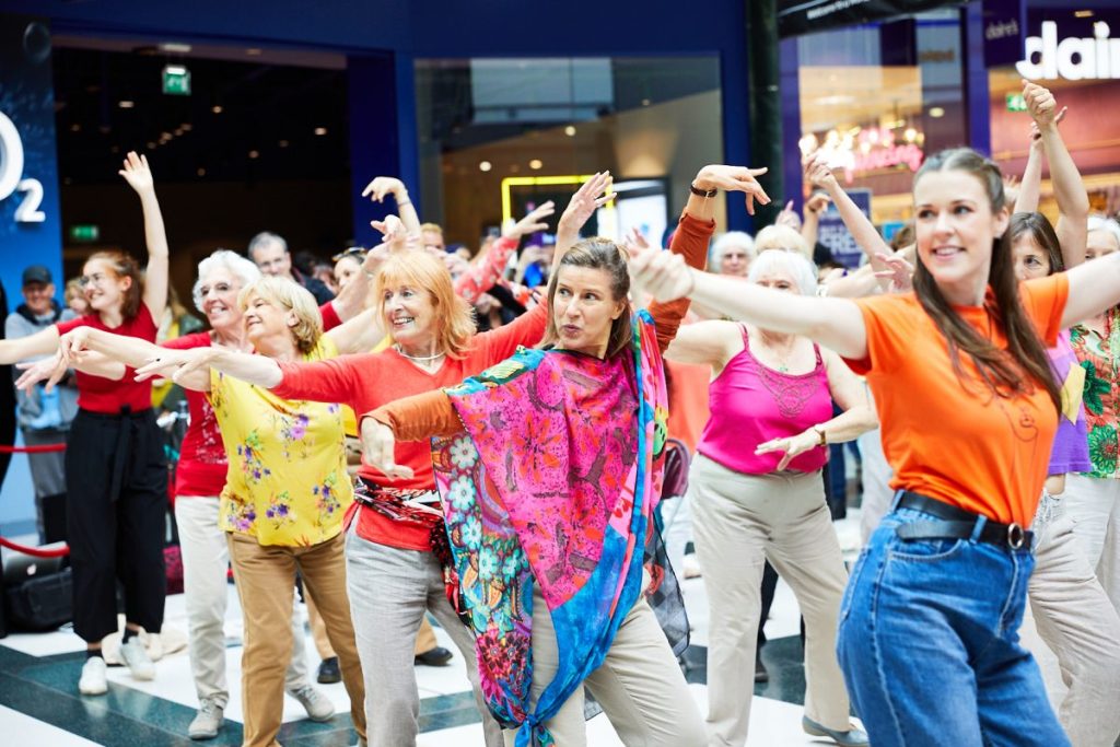 A group of women of different ages dressed in colourful clothing dancing together