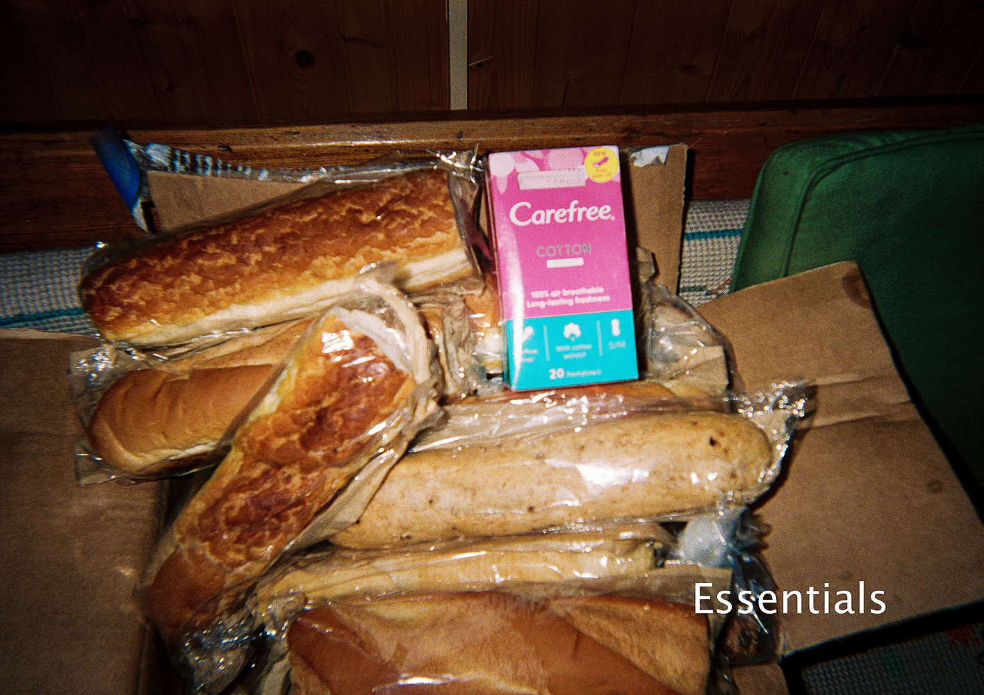 A photograph of a cardboard box full of baguettes with a pink box of pantyliners perched on top.