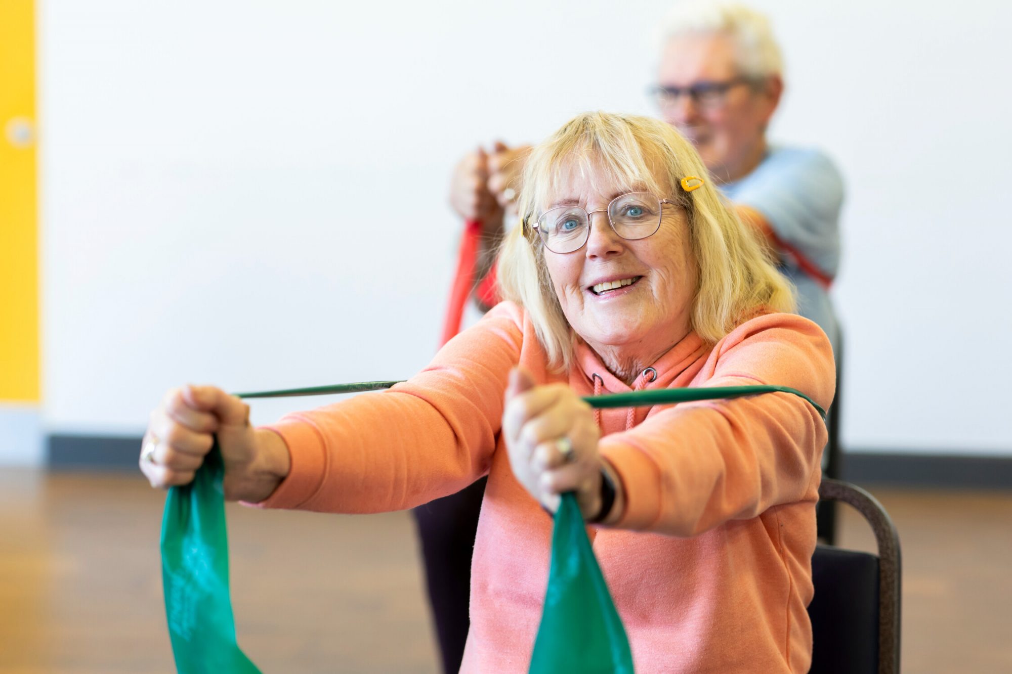 Older woman blonde hair glasses pulling a green exercise band