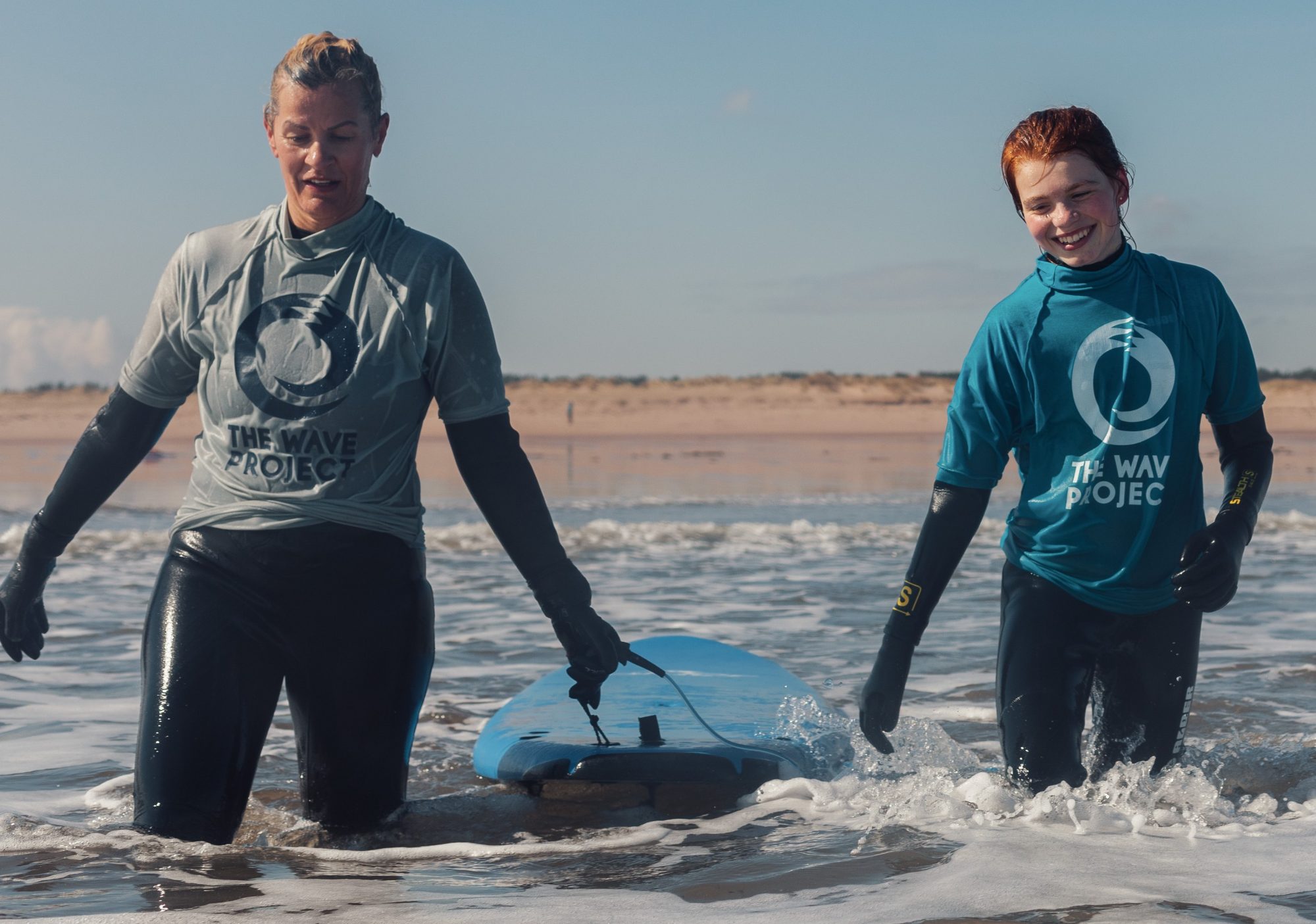 adult and teen in the sea holding a surf board between them