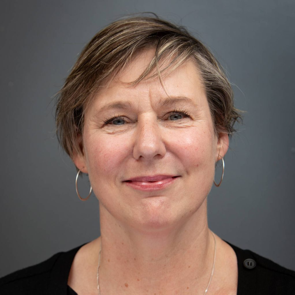Headshot of Amelia Wakeford smiling with a grey background.